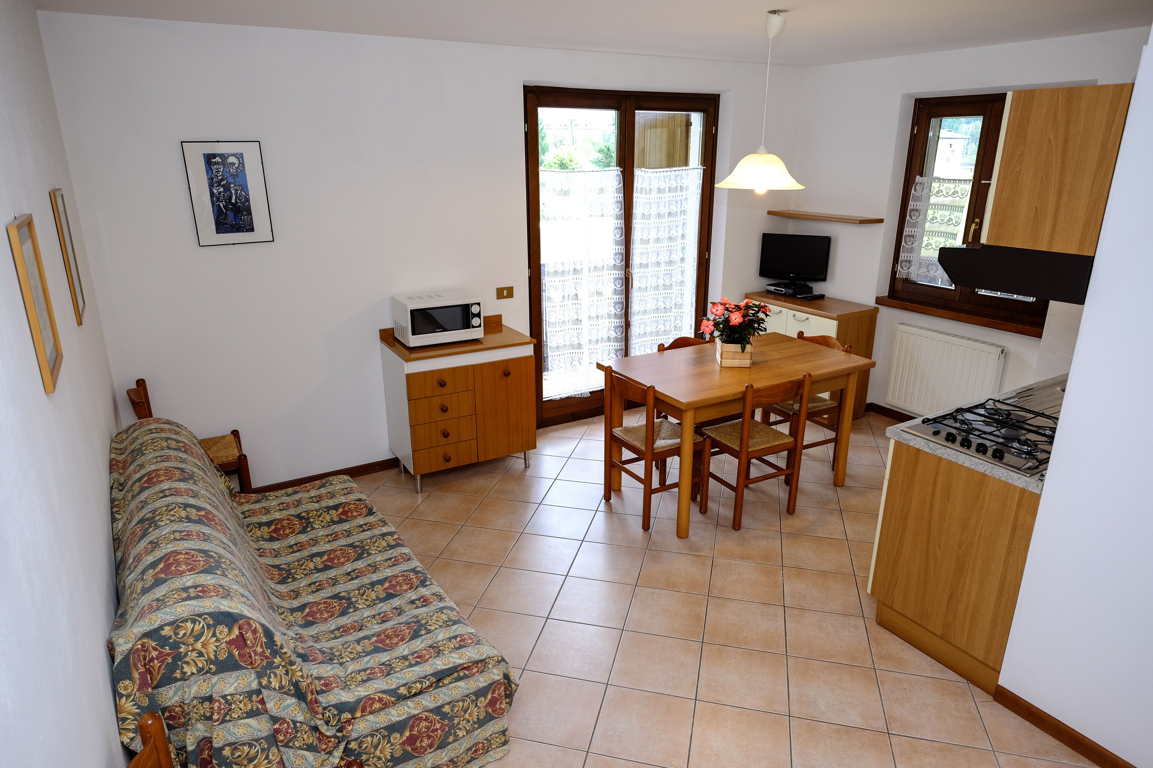 Un espacio habitable pequeño con sofá, mesa de comedor con sillas, kitchenette con estufa, televisor y ventana con cortinas.