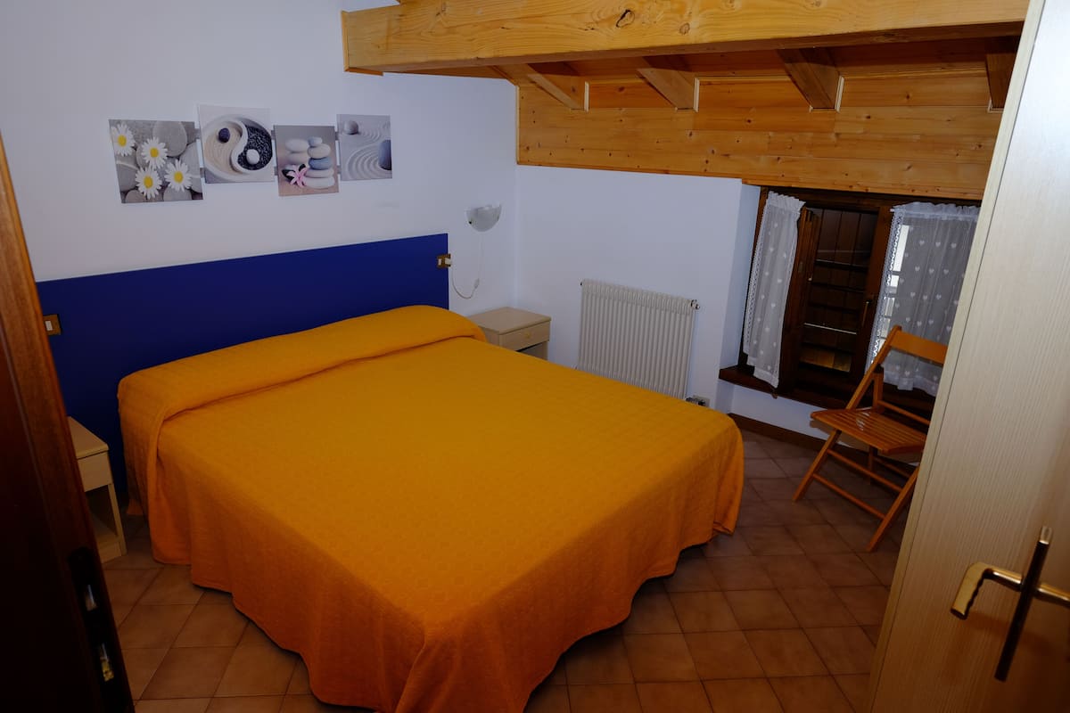 Une chambre avec un lit simple, un plafond en bois, un radiateur et une fenêtre avec des rideaux.