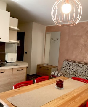 A compact kitchen with a microwave, a wooden dining table with a placemat, and a red chair. - Residence Alessio (Ledro)