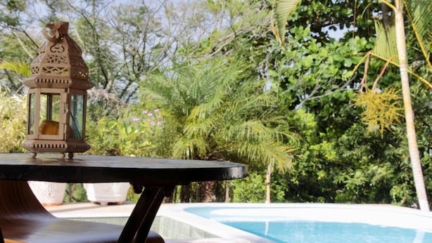 Une table placée au bord de la piscine, agrémentée d’une lanterne, et entourée d’une végétation luxuriante et d’une piscine aux eaux cristallines.