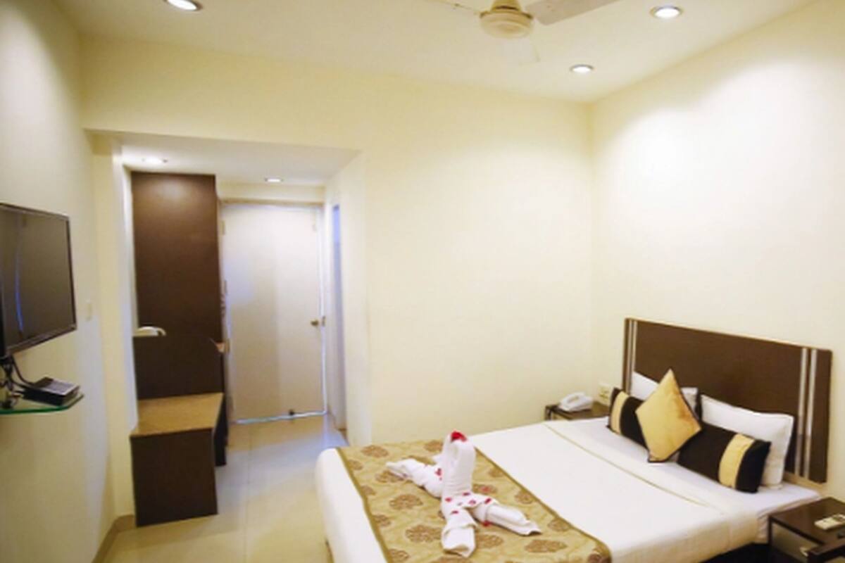 Quarto de hotel com cama, mesa de cabeceira, televisão e ventoinha no teto.