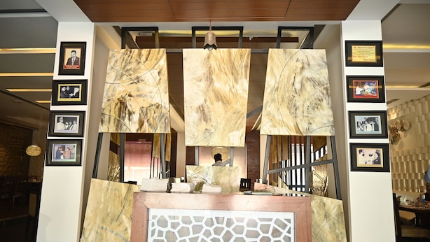 A reception desk with a patterned backdrop, framed photos on the walls, and a wooden ceiling. - Hotel Regency Square (Gwalior)