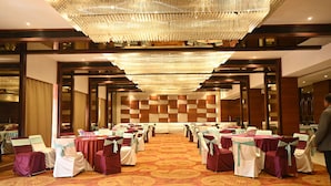 A banquet hall with rows of tables and chairs, a patterned carpet, and a large chandelier. - Hotel Regency Square (Gwalior)