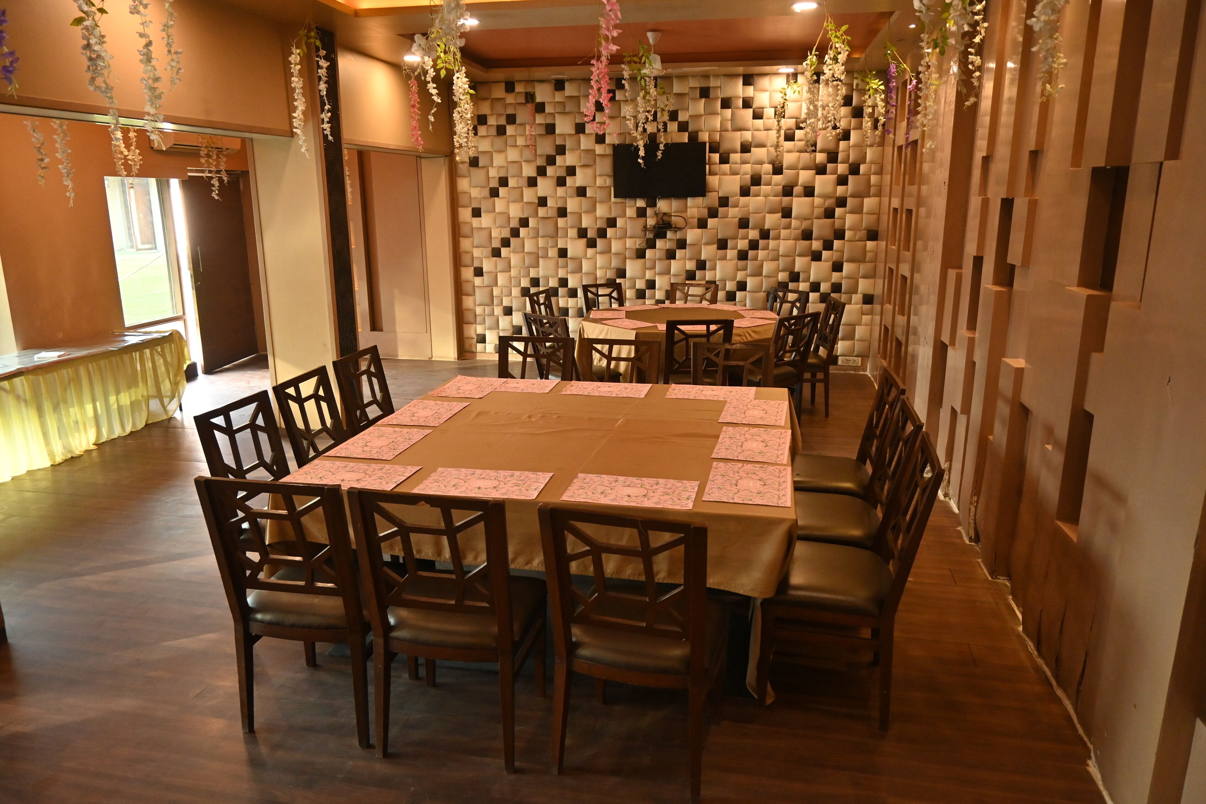 A conference room with a large table, chairs, a TV mounted on the wall, and decorative hanging plants.