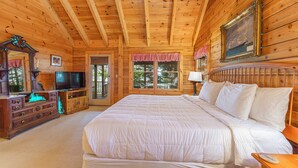 A wooden cabin bedroom with a large bed, a television, and a dresser. - Waterfront log cabin nestled in the woods providing unparalleled privacy (Harpswell)