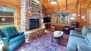 A cozy cabin interior with a stone fireplace, wooden walls, a television, and comfortable seating. - Waterfront log cabin nestled in the woods providing unparalleled privacy (Harpswell)