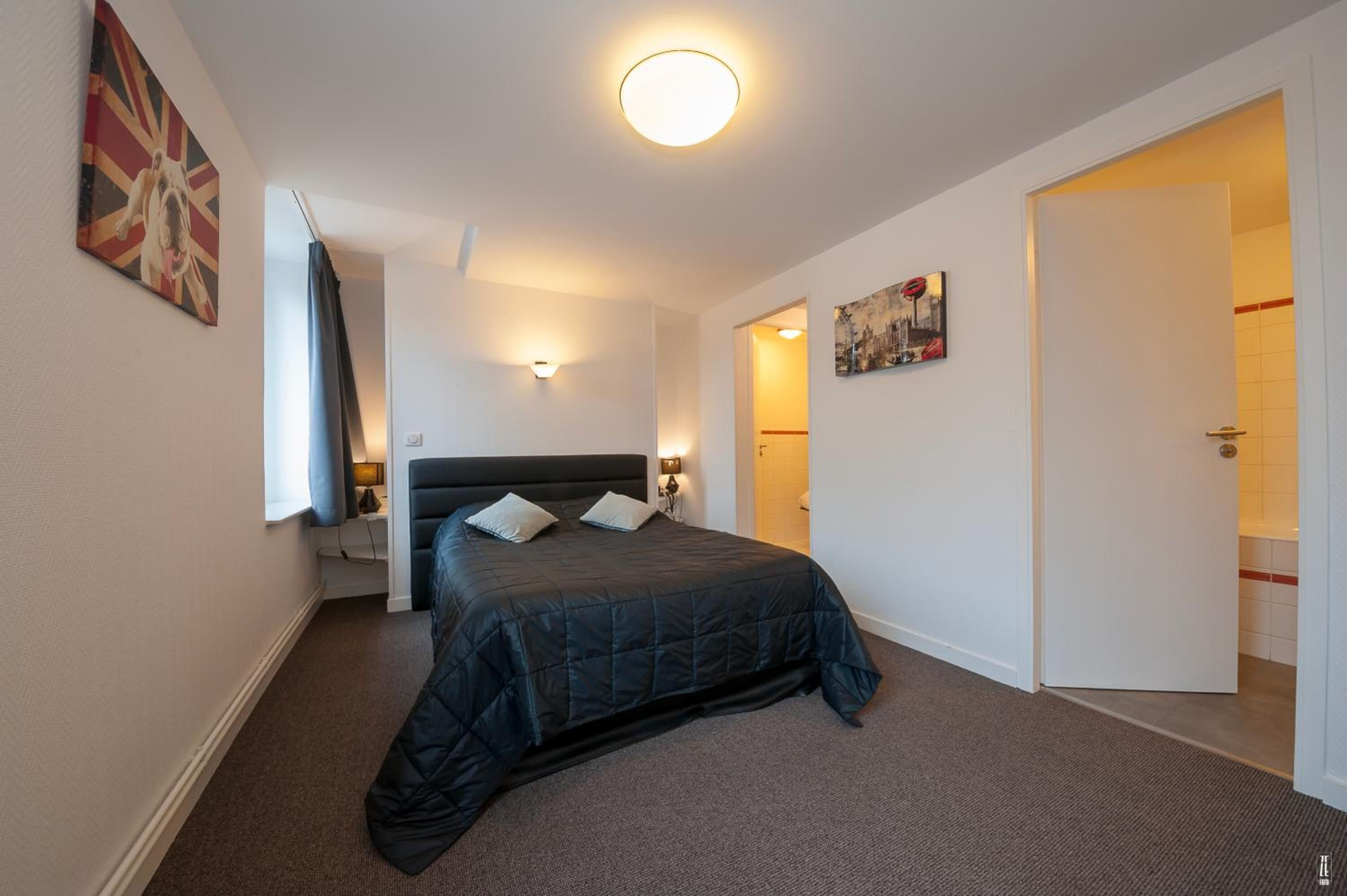 Un dormitorio con cama, mesita de noche, lámpara de pared y puerta que da a otra habitación.