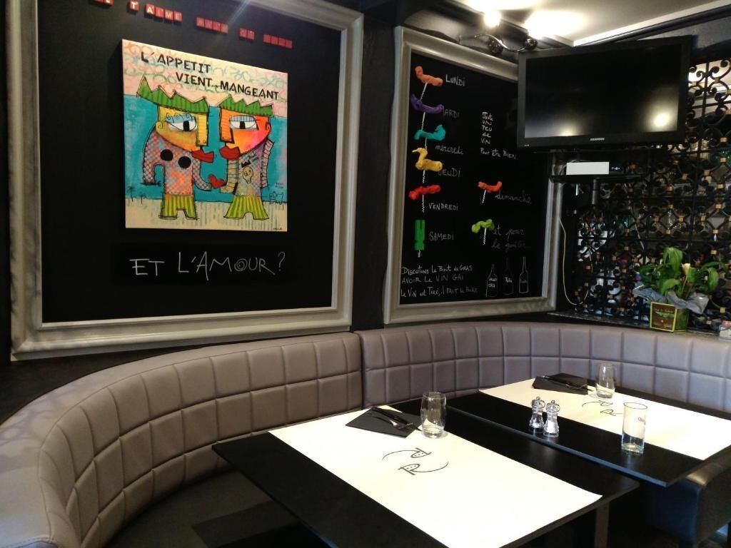 Interior de un restaurante con un menú en pizarra, una televisión y una zona de estar con mesas y cabinas acolchadas.