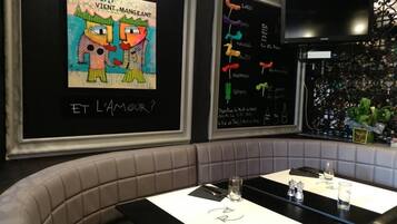 Interior de un restaurante con un menú en pizarra, una televisión y una zona de estar con mesas y cabinas acolchadas.