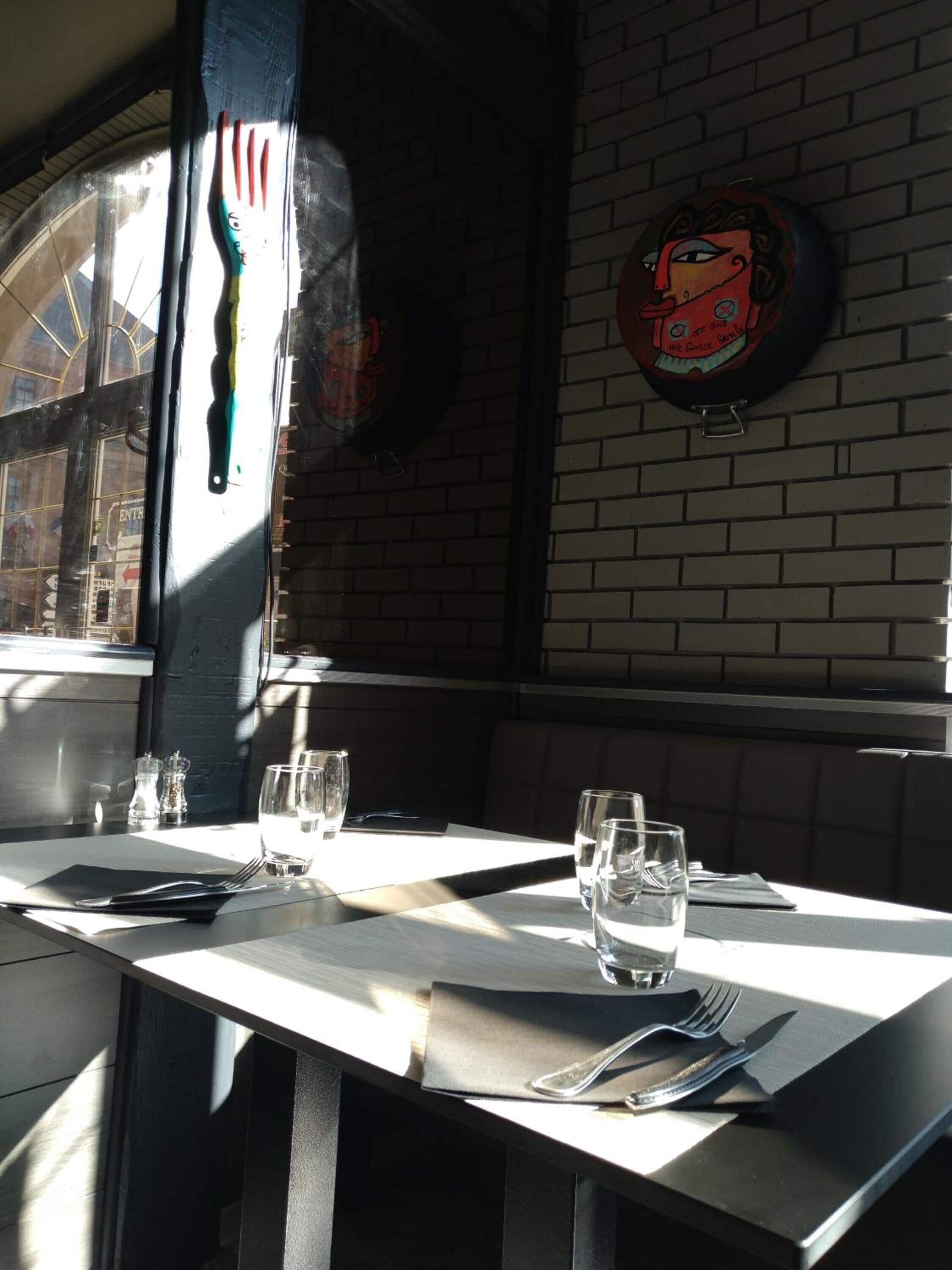 A dining table with a window view, a brick wall, and a painted wall decoration.
