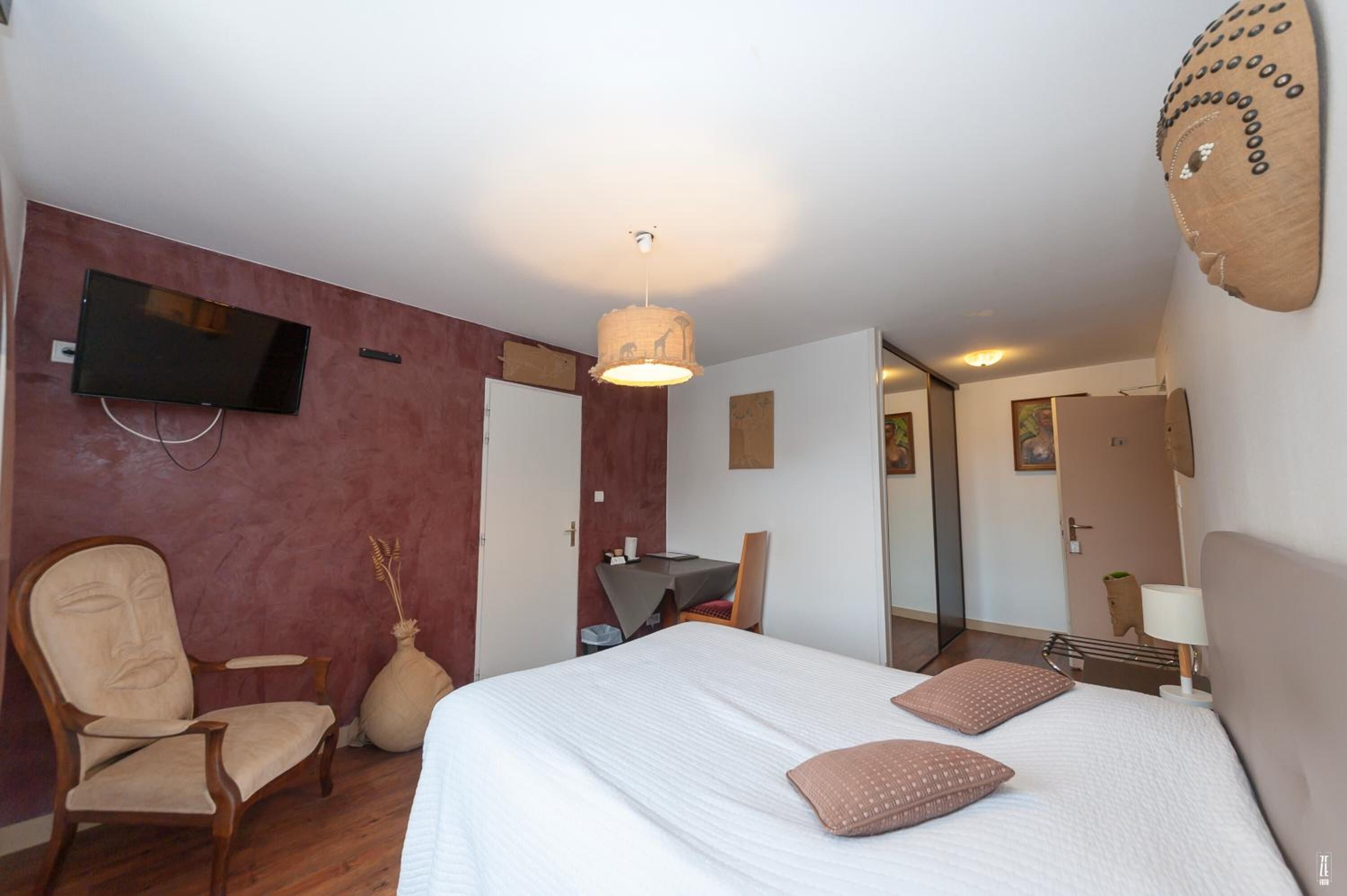 Una habitación de hotel con cama, una silla, un escritorio, un televisor y un espejo.