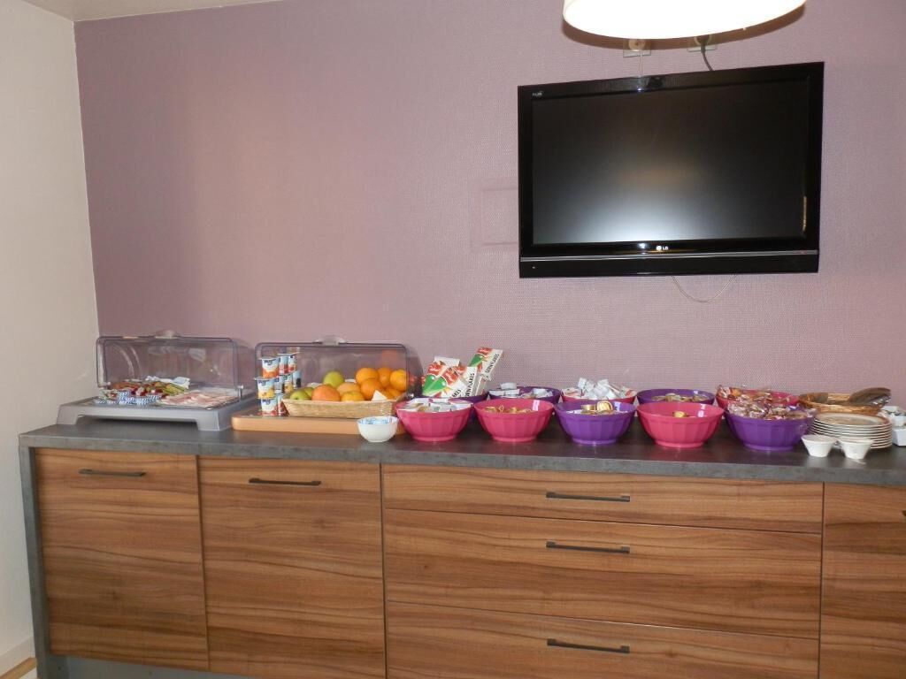 A kitchenette with a flat-screen TV mounted on the wall, a countertop with various food containers and a fruit bowl.