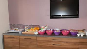 A kitchenette with a flat-screen TV mounted on the wall, a countertop with various food containers and a fruit bowl.