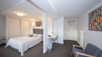 A hotel room with a bed, a desk, a chair, and a radiator.