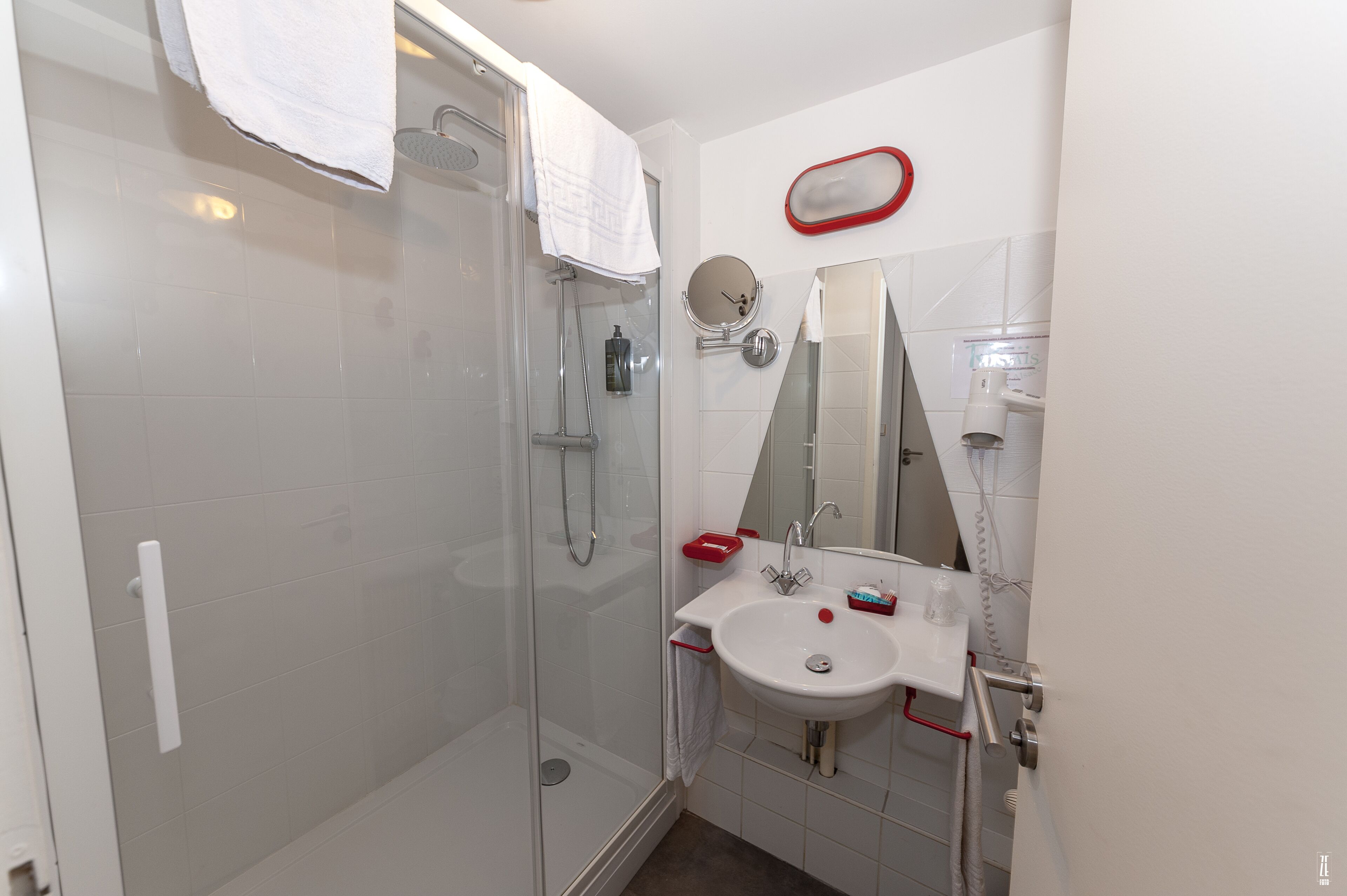 Un baño moderno con ducha envuelta en vidrio, un lavamanos blanco y un espejo de marco rojo.