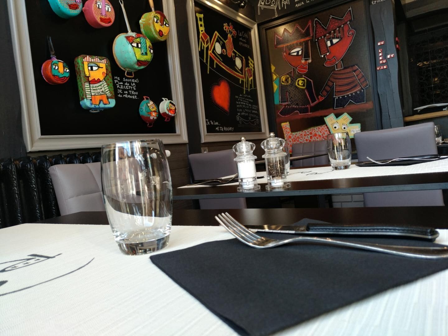 A restaurant interior with a table set for two, featuring a clear glass, salt and pepper shakers, and a menu.