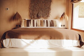 A bed with a brown and white striped blanket, two hanging wall decorations, and a small thermostat on the wall. - Nomad Xabia Port (Javea)