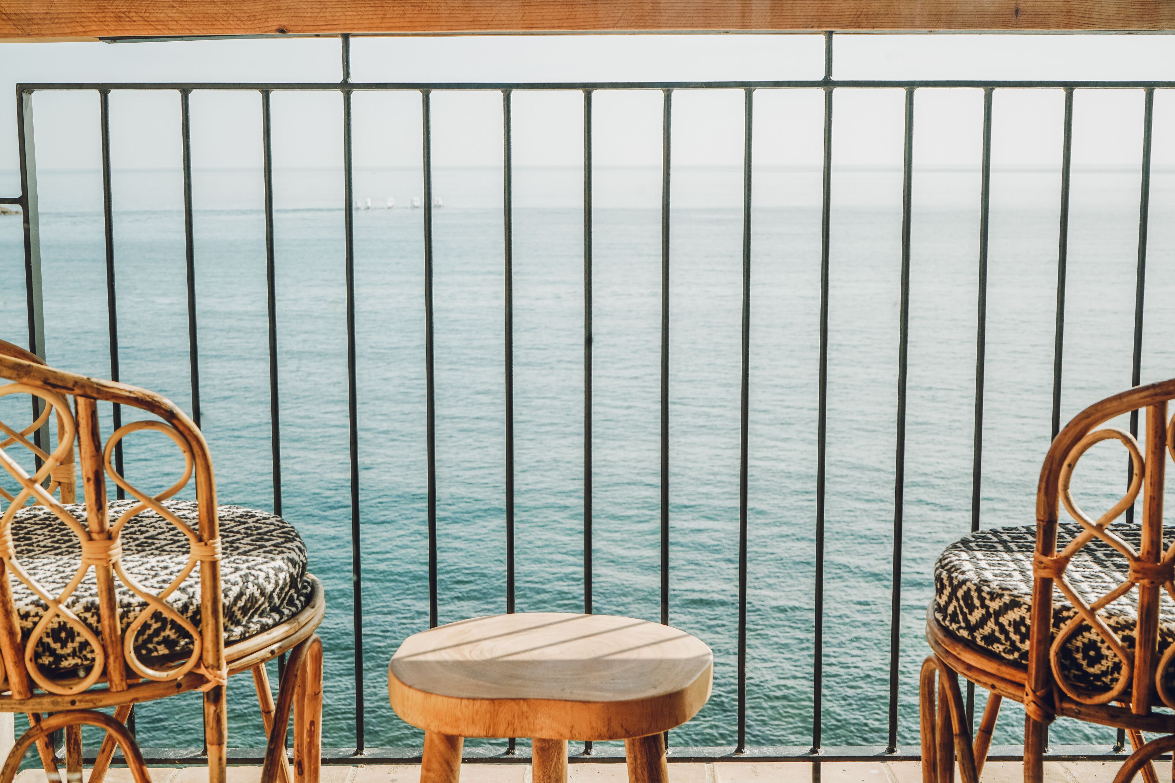 A balcony with two wicker chairs and a small wooden table, overlooking a calm sea.