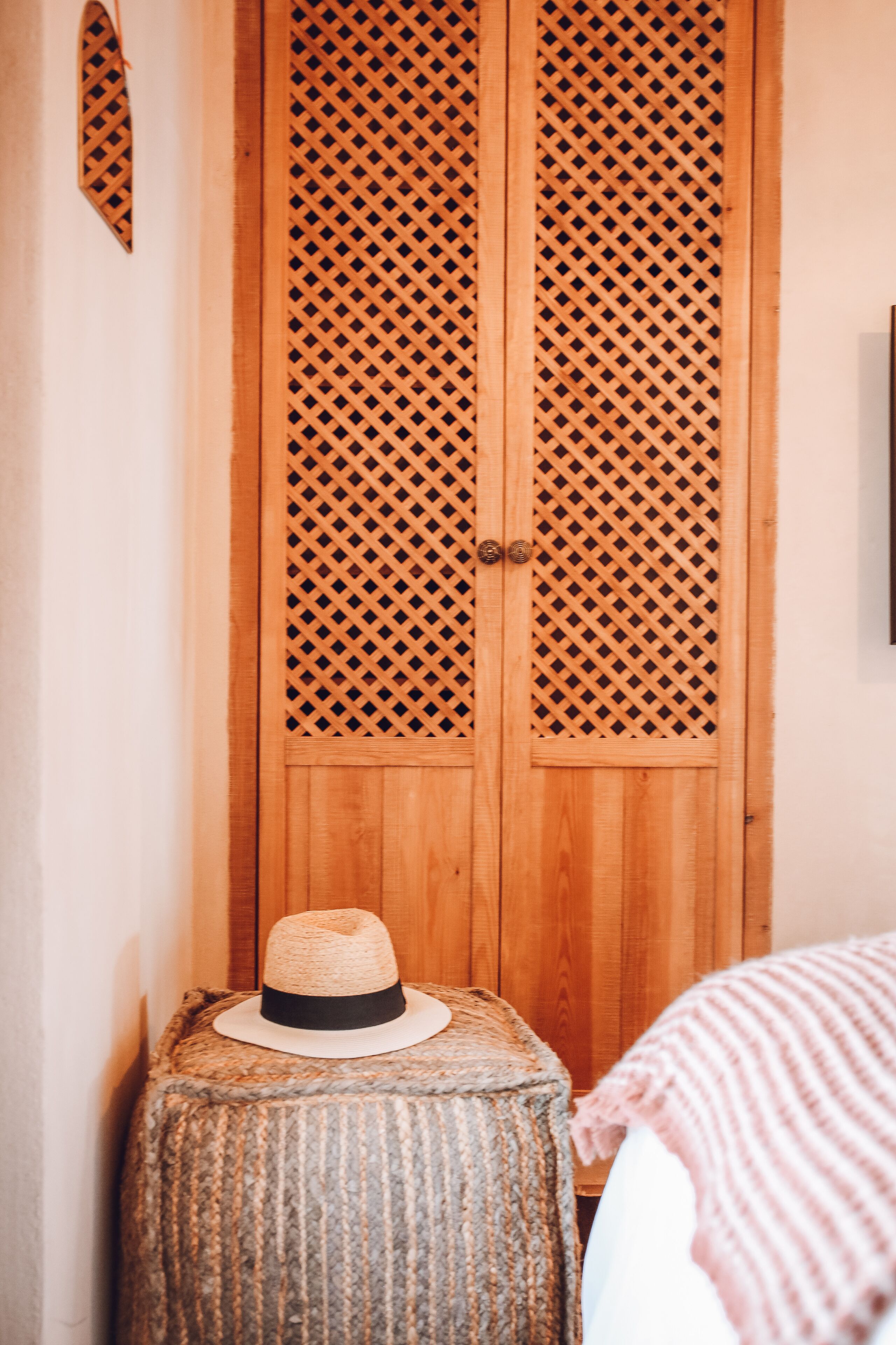 A wooden wardrobe with a lattice design, a woven stool, and a straw hat on top.