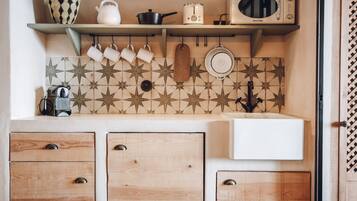 Una cocina con armarios de madera, microondas, hervidor y tazas colgando.