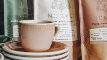 A stack of white plates with a white cup on top, and two coffee bags labeled 'NOMAD' in the background.