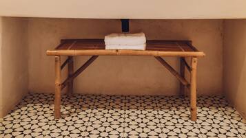 A bathroom with a round mirror, two pendant lights, a wooden bench, and a tiled floor.