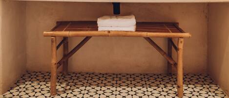 Une salle de bain avec un miroir rond, deux lampes suspendues, un banc en bois et un sol carrelé.