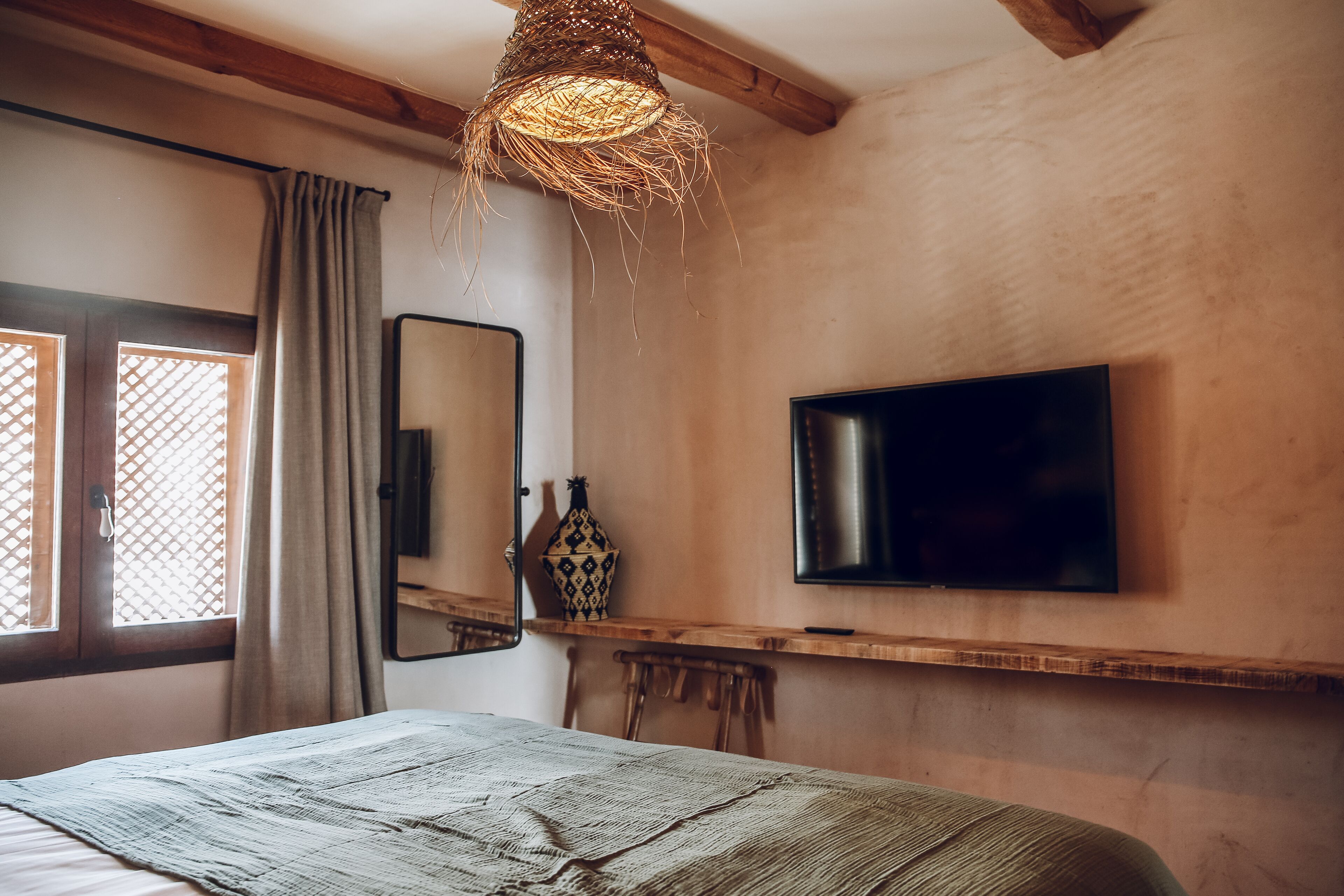 Un dormitorio con cama, televisor montado en la pared, espejo y ventana con cortinas.