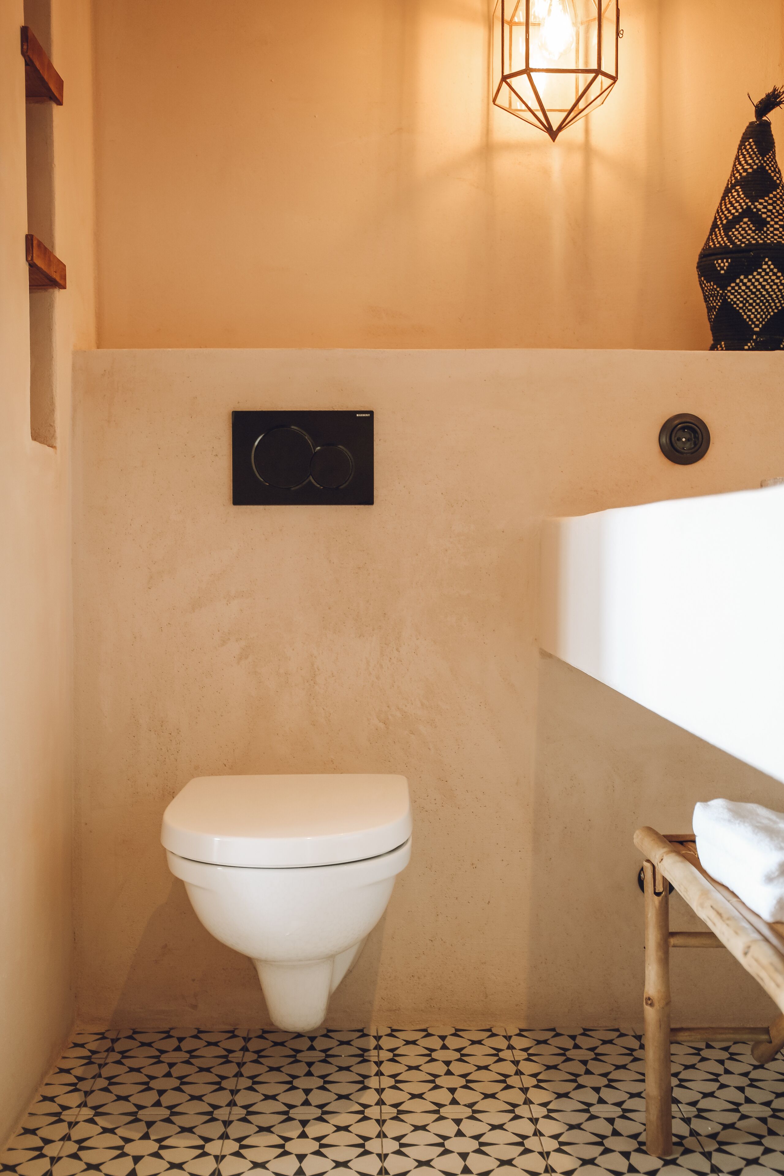 A bathroom with a white toilet, a black and white patterned floor, a wall-mounted light fixture, and a towel rack.