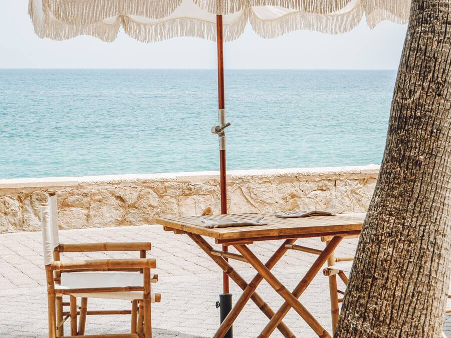 Une scène de plage avec une table et une chaise en bois sous un parasol blanc, donnant sur la mer.