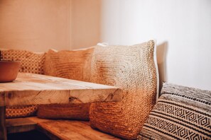 A wooden table with a bowl, a woven sofa with patterned cushions, and a woven throw blanket. - Nomad Xabia Port (Javea)