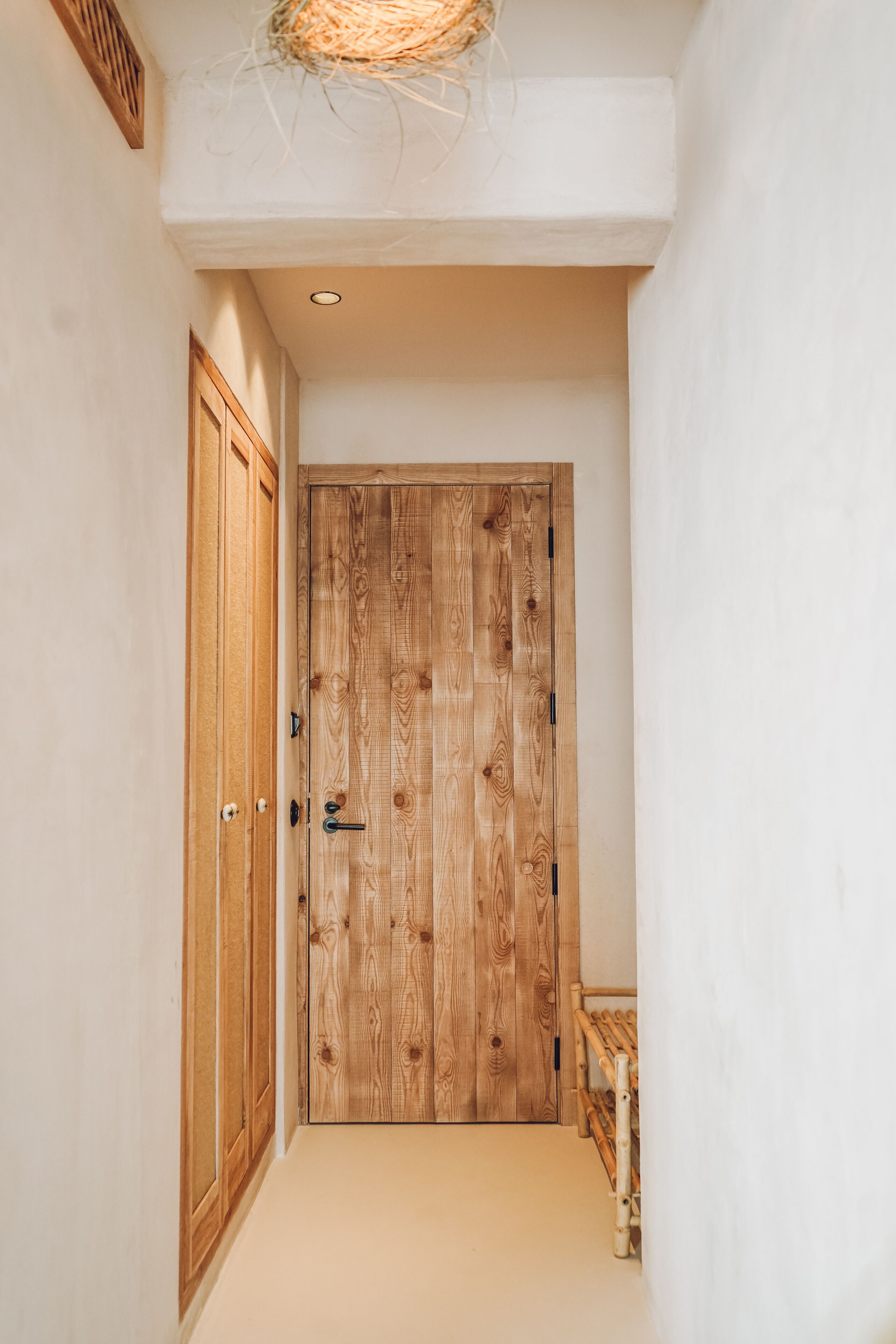 A hallway with a wooden door, a small bench, and a hanging basket.