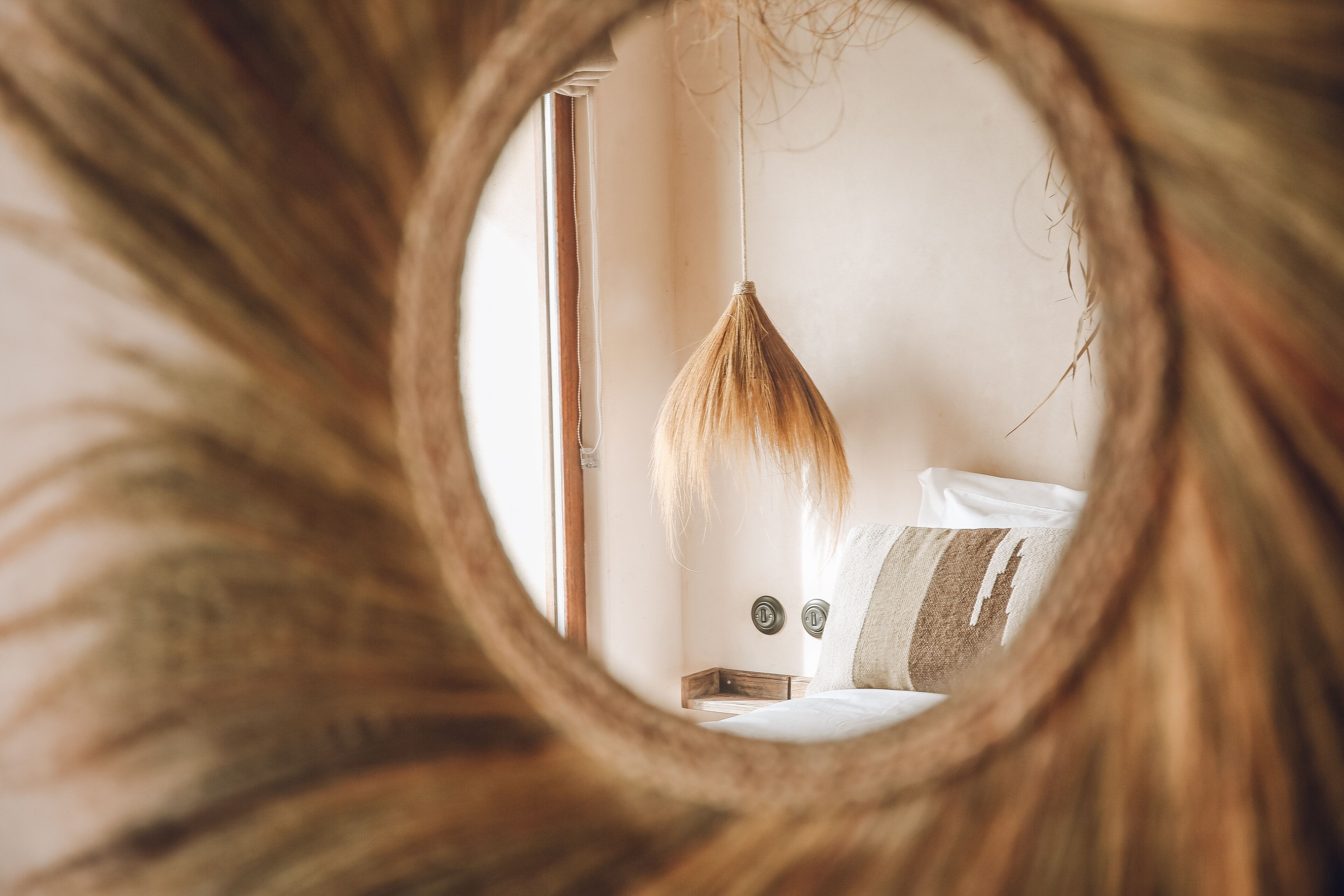Ein Schlafzimmer mit einer Pendelleuchte, einem Bett mit Kissen und einem Spiegel, der einen Teil des Raumes widerspiegelt.
