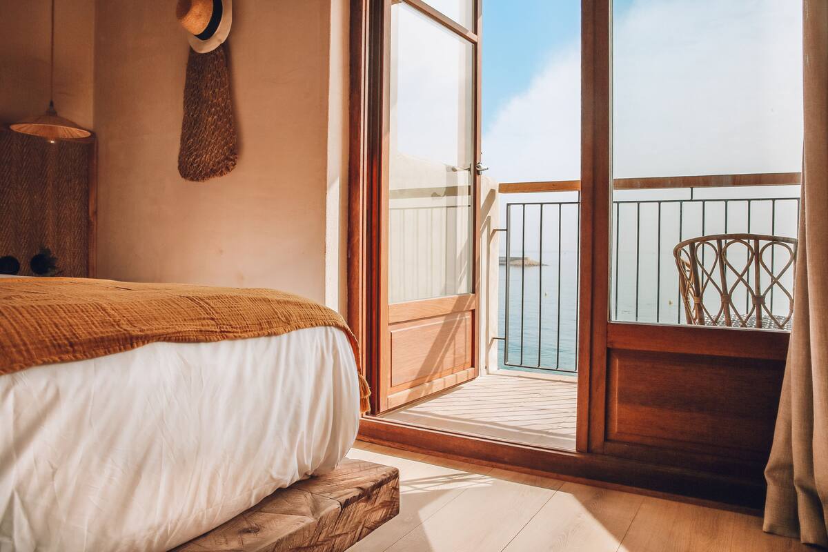 Ein Schlafzimmer mit einem Bett, einer hölzernen Bank, einem aufgehängten Hut und einem Balkon mit Geländer.