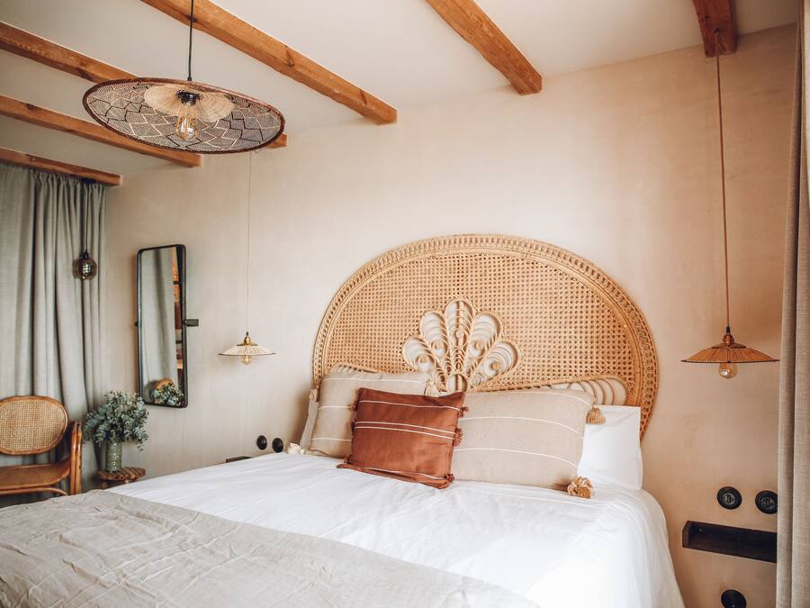 A bedroom with a large bed, wooden beams, a woven headboard, and a hanging light fixture.