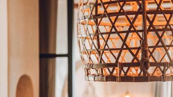 Une lampe en osier ornée d’un motif géométrique, un lit avec une literie blanche et une chaise en bois.