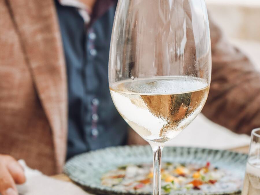 A table with a glass of white wine, a plate of food, and a napkin.