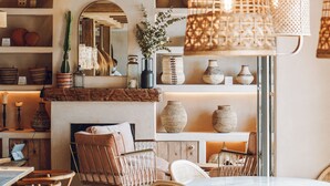 Un interior acogedor con muebles de mimbre, una chimenea, estantes con adornos y lámparas colgantes de mimbre.