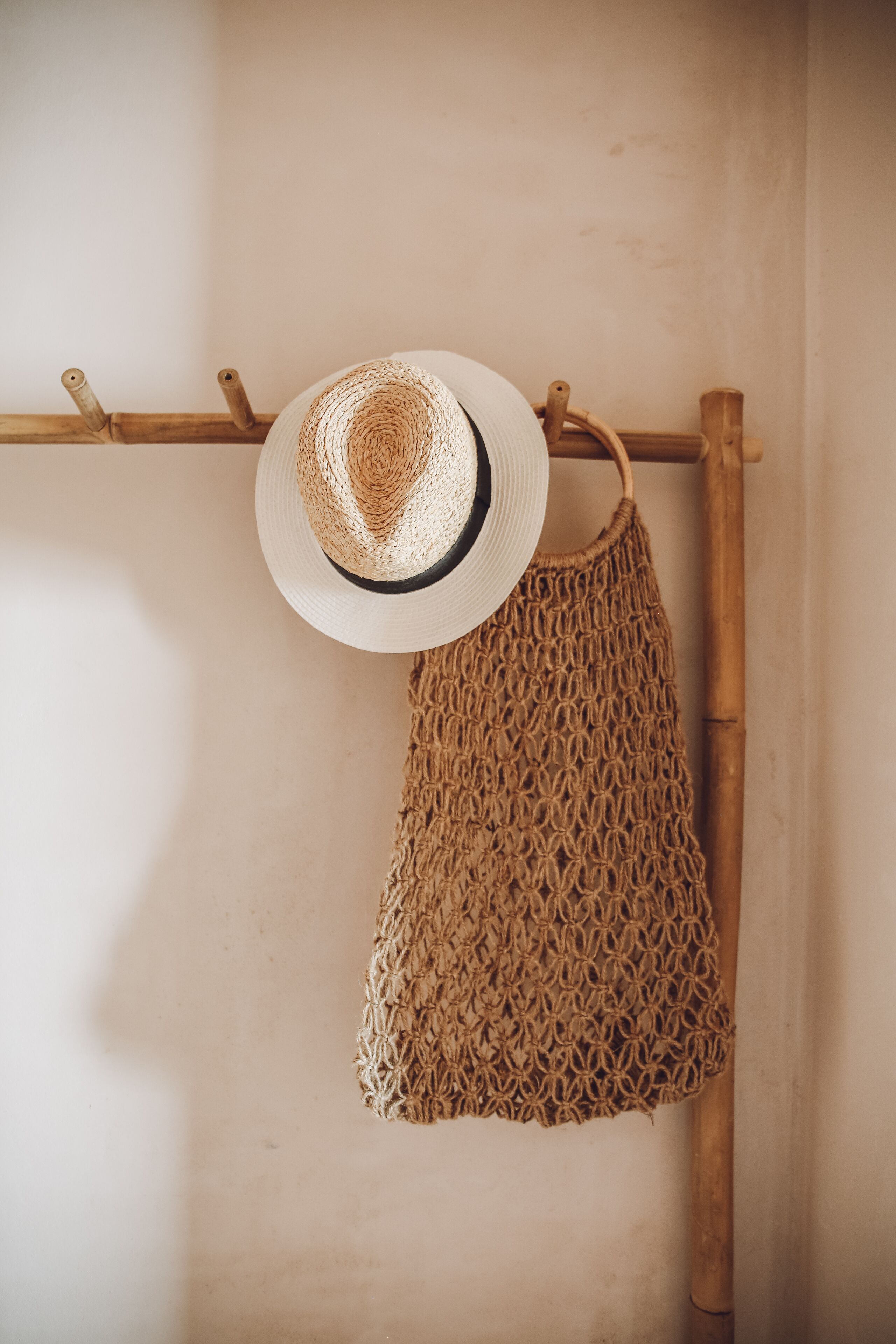 A straw hat and a woven bag hanging on a wooden rack against a plain wall.