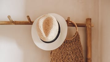 A straw hat and a woven bag hanging on a wooden rack against a plain wall.