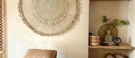 A bedroom with a bed, a woven wall hanging, shelves with rolled towels, and a small shelf with toiletries.
