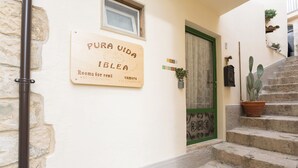 A building entrance with a sign for rooms for rent, a green door, a staircase, and a cactus plant.