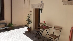 A small outdoor seating area with two wooden chairs and a table, a potted plant, and a small bench.