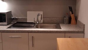 A kitchen with white cabinets, a microwave, a sink, and a wooden table. - Riverside 4 (Maidstone)
