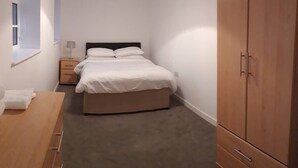 A bedroom with a bed, bedside table, lamp, wardrobe, and a window. - Riverside 4 (Maidstone)