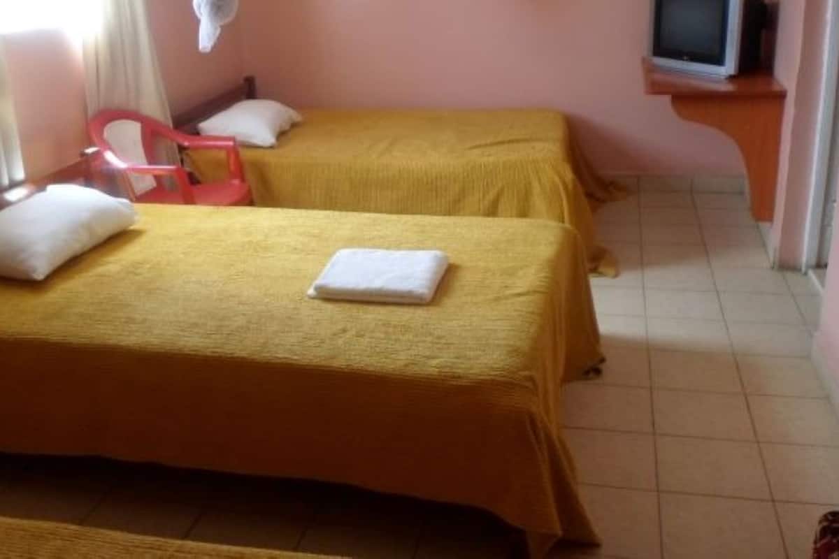 Une chambre avec deux lits, chacun recouvert d’une couvre-lit jaune et agrémenté d’oreillers blancs. Un téléviseur est posé sur un meuble en bois, à droite.