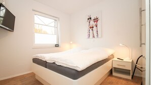A modern bedroom with a bed, bedside table, lamp, and artwork on the wall. - Charming apartment in Greetsiel - Leystuuv (Greetsiel)