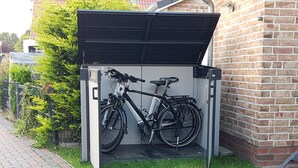 A bicycle storage unit with a roof, located next to a brick building. - Charming apartment in Greetsiel - Leystuuv (Greetsiel)