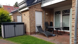 A patio with a table and chairs, a shed, and a door. - Charming apartment in Greetsiel - Leystuuv (Greetsiel)