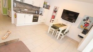 A compact kitchen with white cabinets, a built-in oven, and a wooden countertop. A dining area with a table and chairs is adjacent to the kitchen. - Charming apartment in Greetsiel - Leystuuv (Greetsiel)